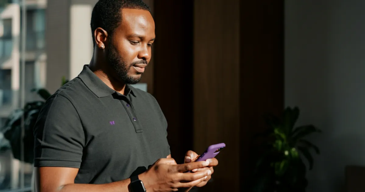 Homem focado utiliza smartphone em ambiente corporativo com iluminação natural